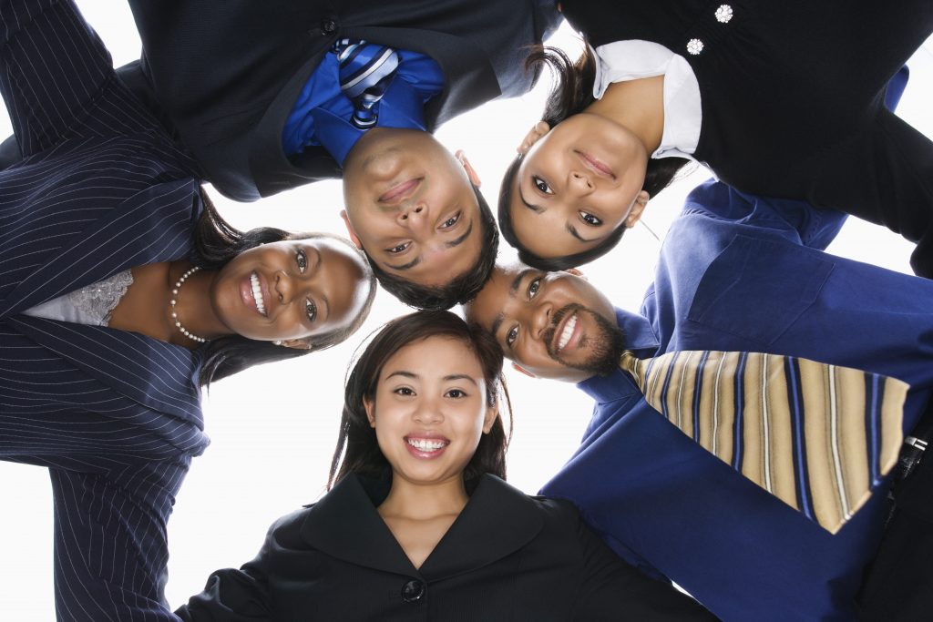 Low angle portrait of multi-ethnic business group of men and women in huddle looking at viewer.